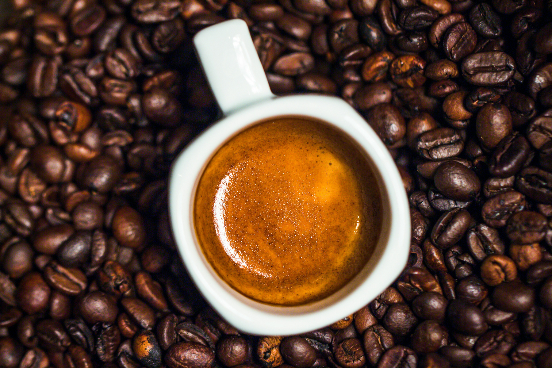 Auto-generated description: A cup of espresso is surrounded by a bed of coffee beans.