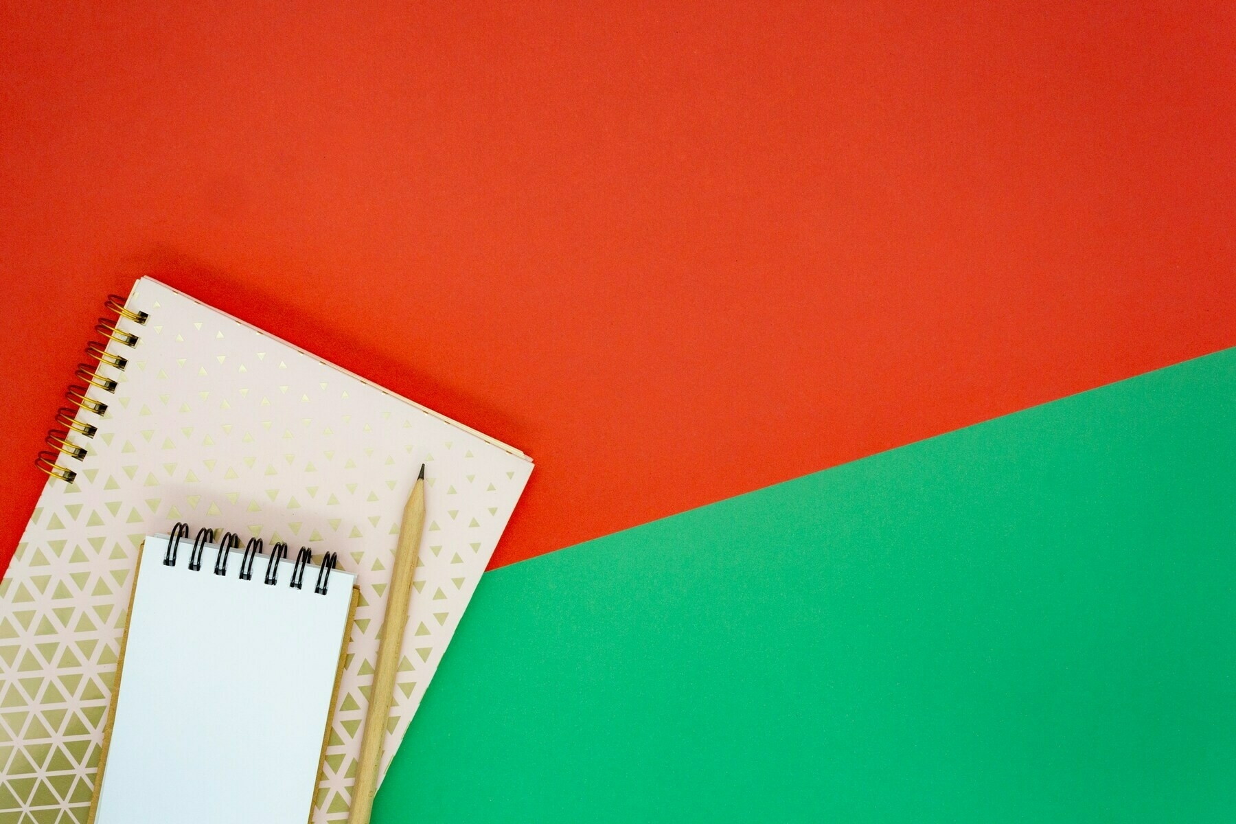 Auto-generated description: A spiral notebook and a pencil are placed on a red and green background.