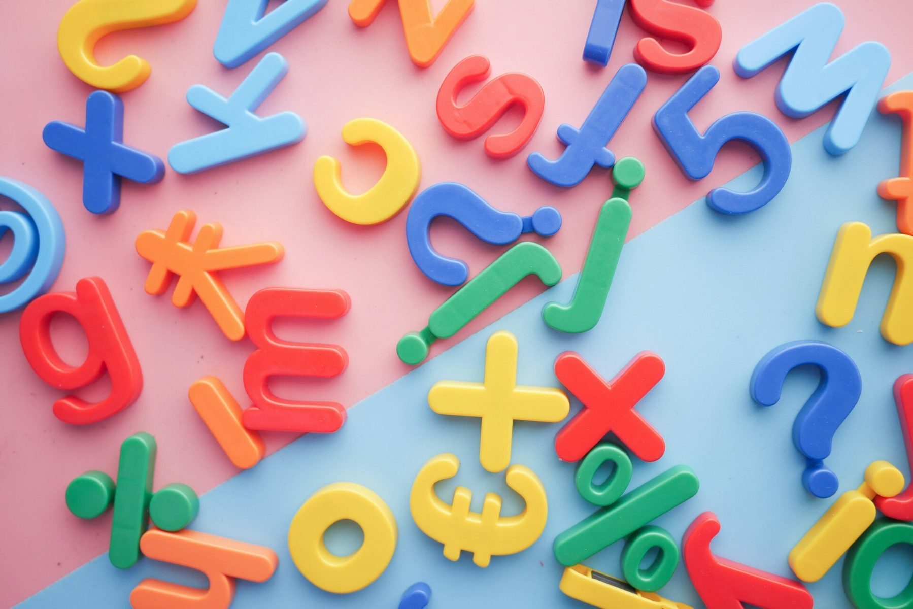Auto-generated description: Colorful plastic letters and symbols are scattered across a divided pink, blue, and purple background.