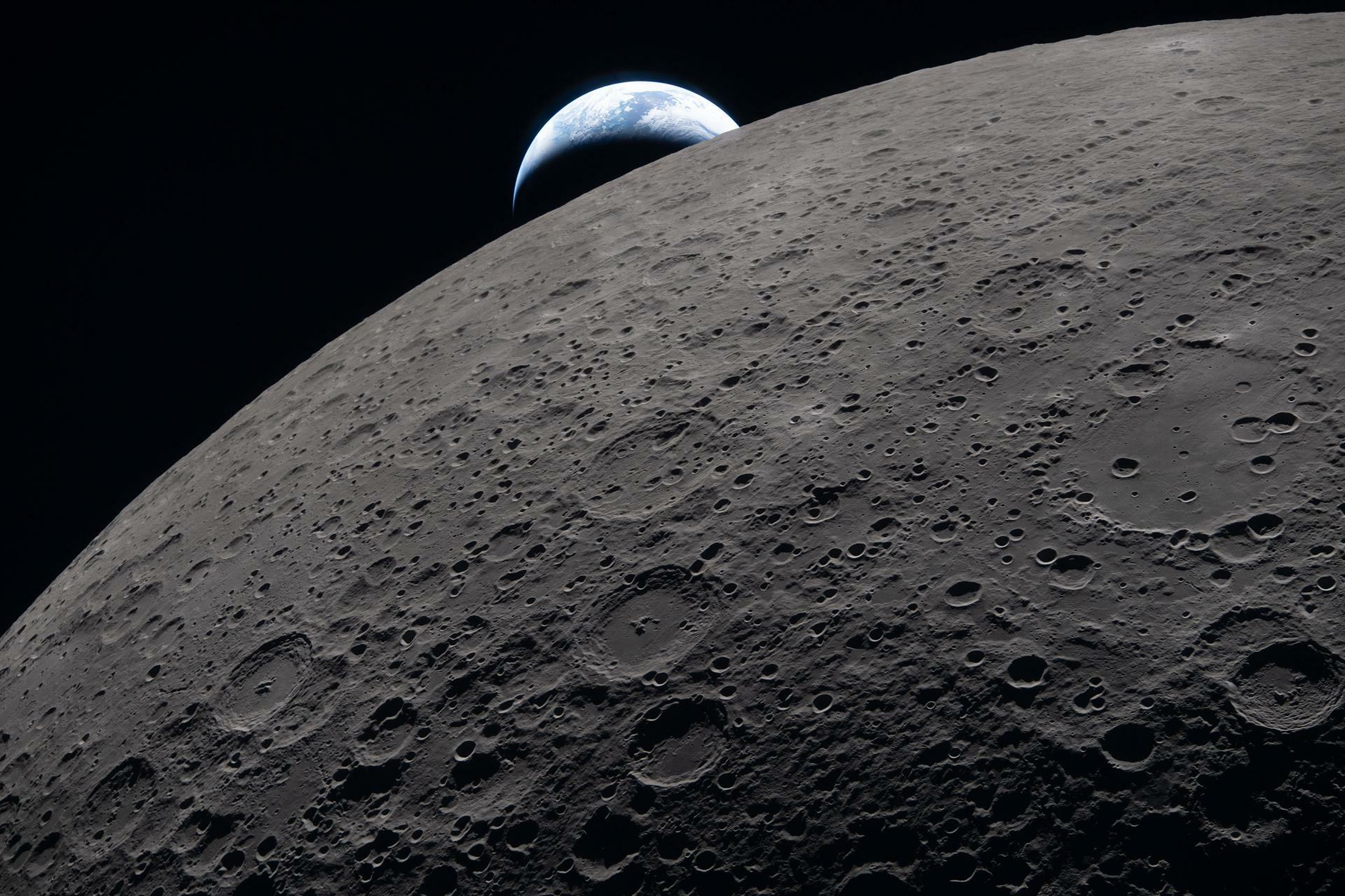Auto-generated description: A view of Earth rising over the rugged, cratered surface of the Moon.